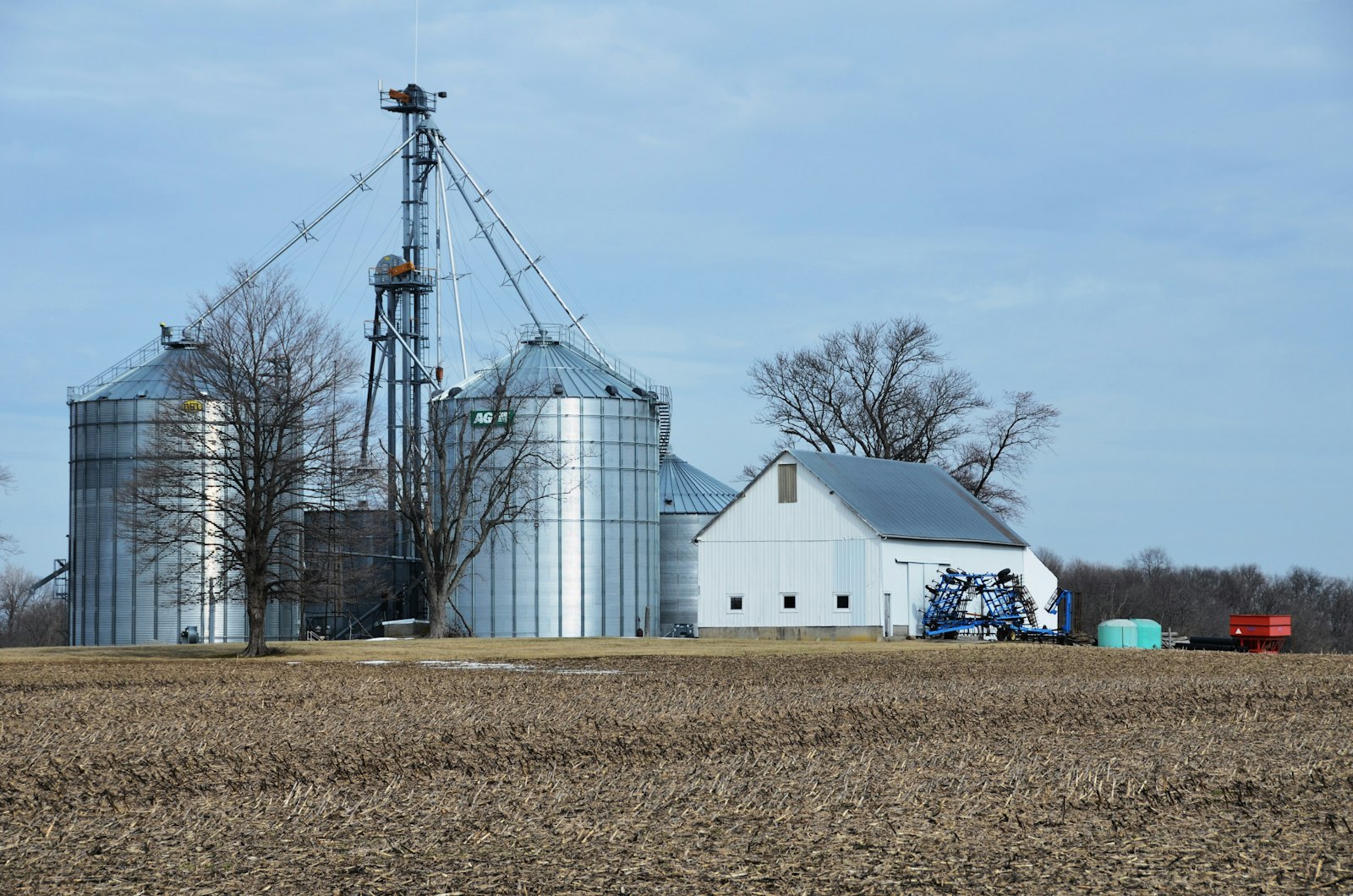 A large white barn with silver grain storage bins on a farm