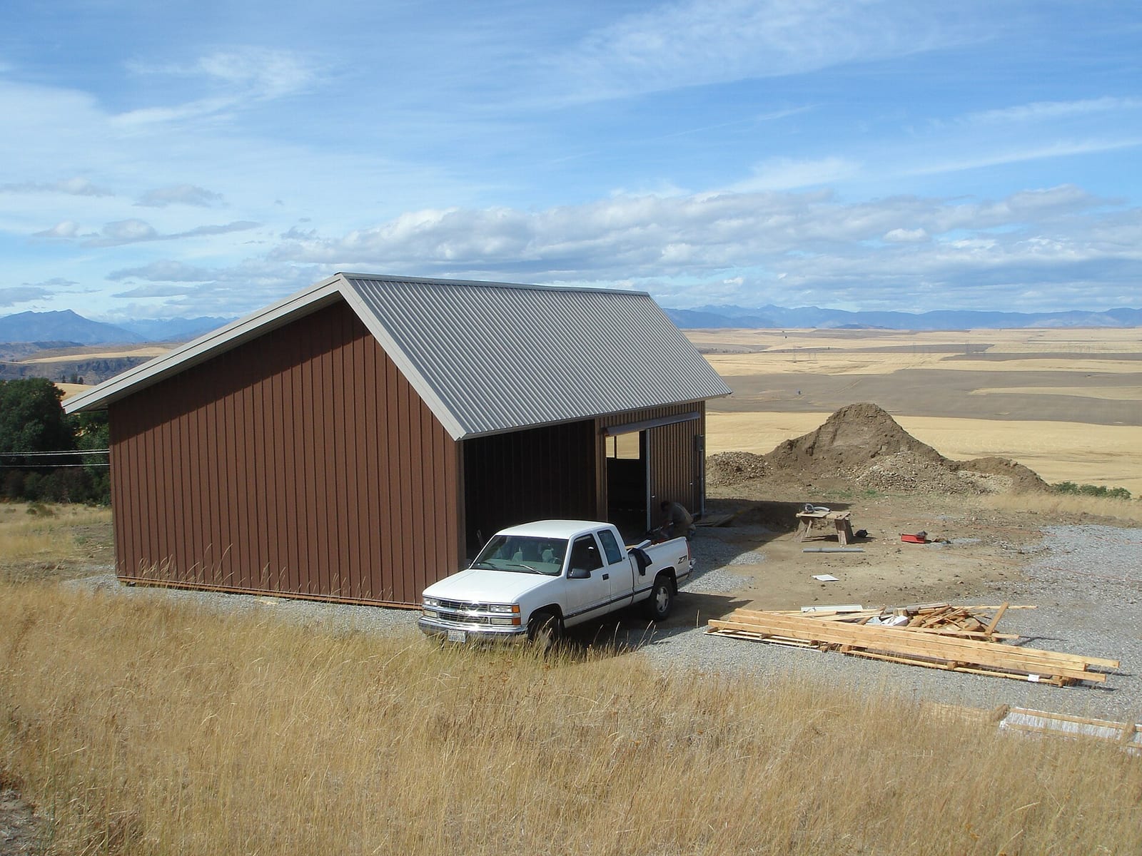 A pole barn with metal siding and a gable roof standing in an open field