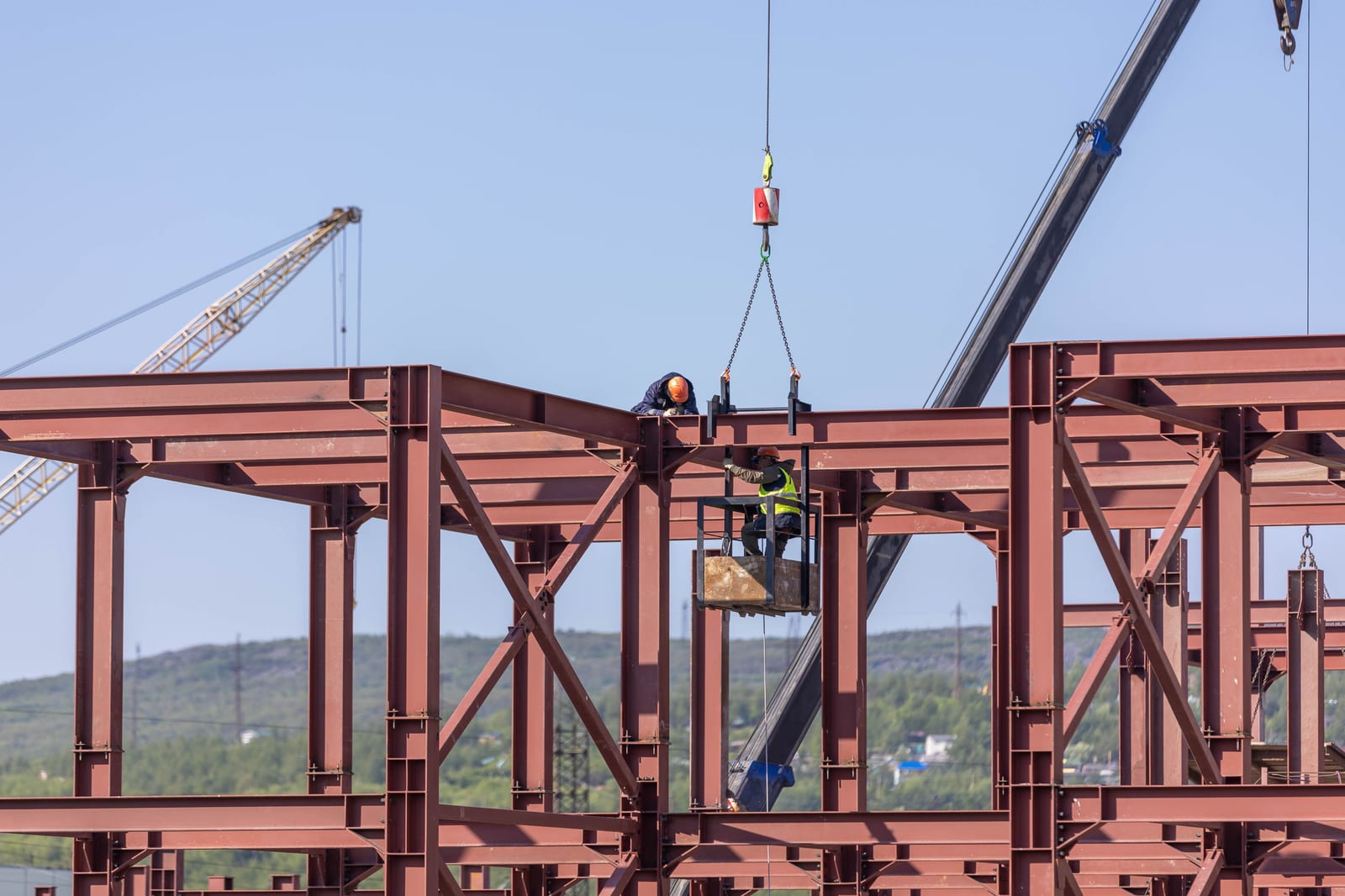 Construction workers assembling a steel frame structure with cranes